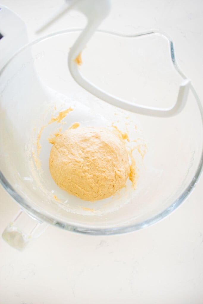 sourdough pretzel bun dough in a glass stand mixing bowl on a marble counter.