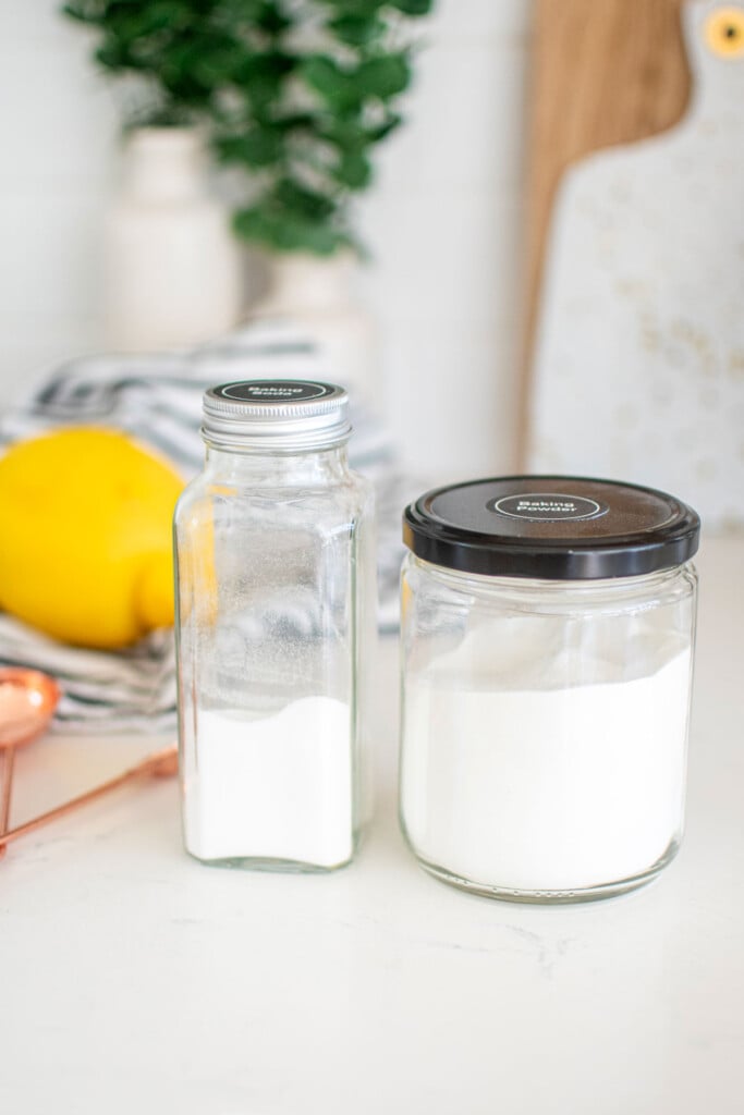 glass jars of baking soda and baking powder on the counter with a fresh lemon.