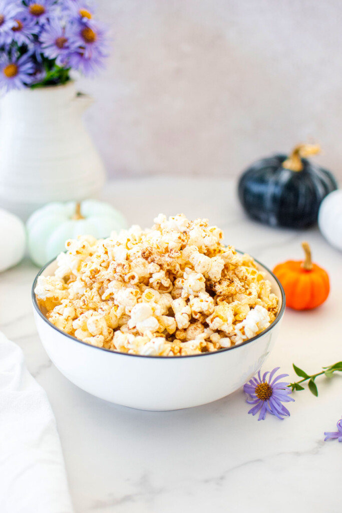 brown butter pumpkin spice popcorn in a bowl on a marble countertop with pumpkins and flowers.