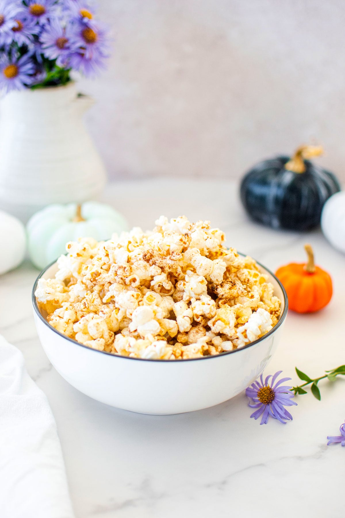 brown butter pumpkin spice popcorn in a bowl on a marble countertop with pumpkins and flowers.
