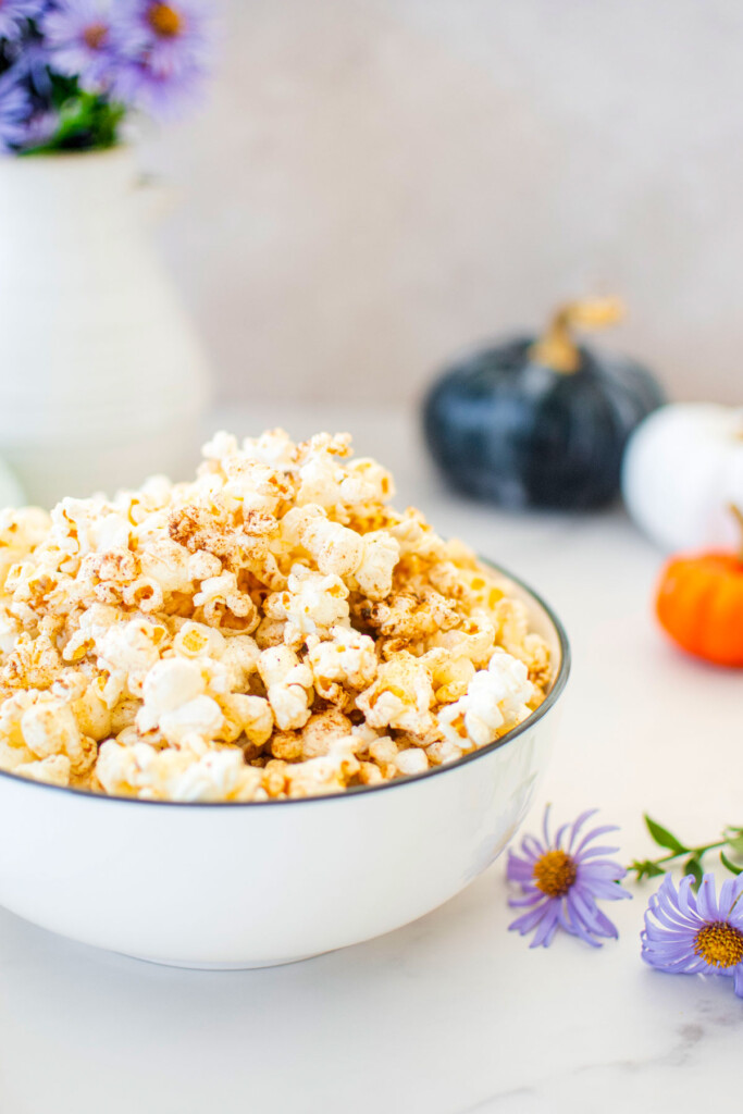 brown butter pumpkin spice popcorn in a bowl on a marble countertop with flowers and pumpkins.