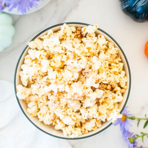 brown butter pumpkin spice popcorn in a bowl on a marble countertop with pumpkins and flowers.