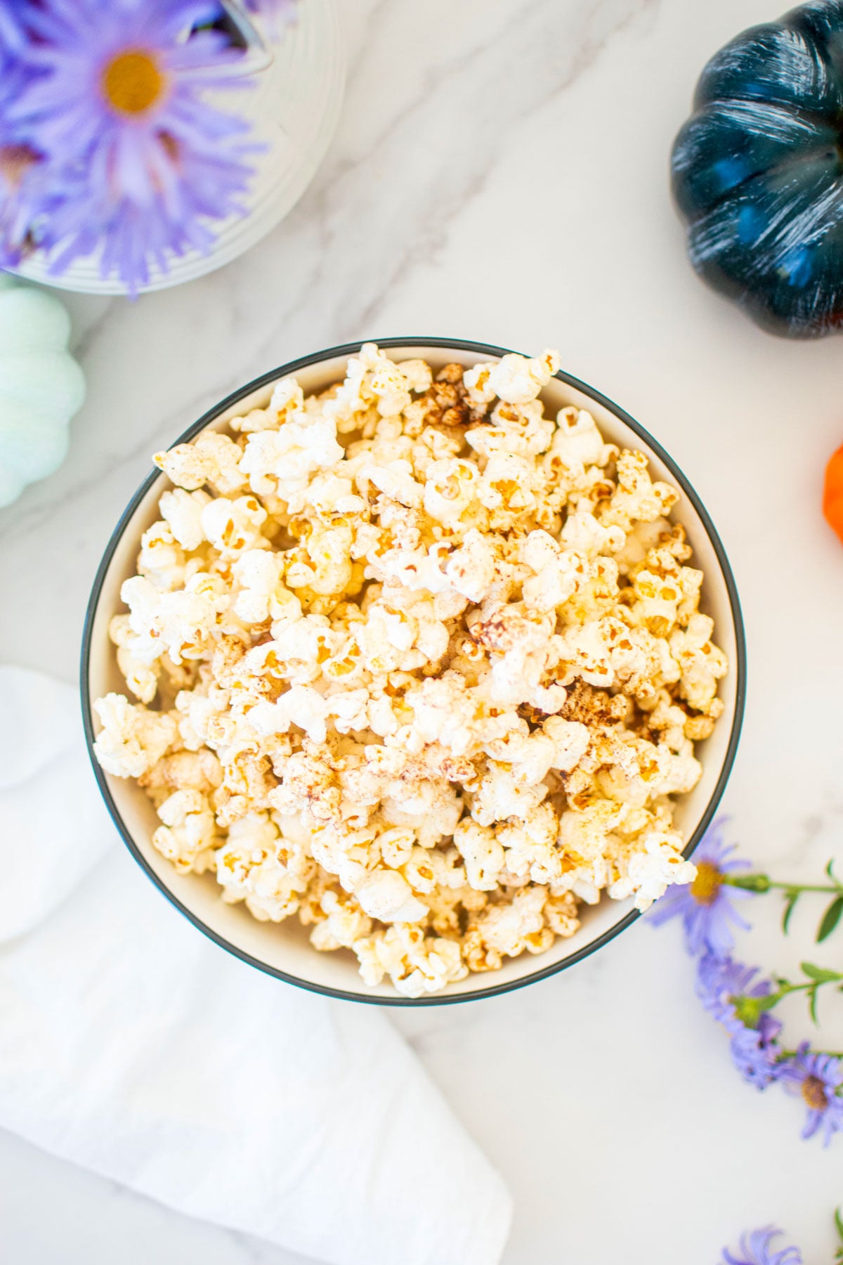 brown butter pumpkin spice popcorn in a bowl on a marble countertop with pumpkins and flowers.