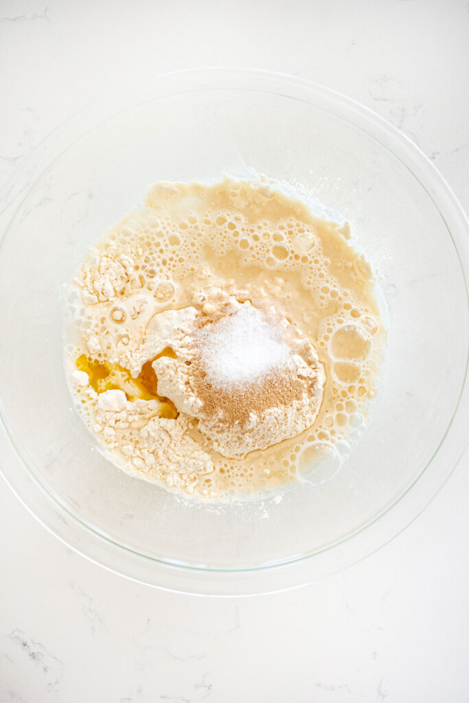 ingredients for pan pizza dough in a glass mixing bowl on a white marble counter.