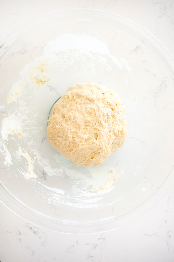 pan pizza dough in a glass mixing bowl on a white marble counter.