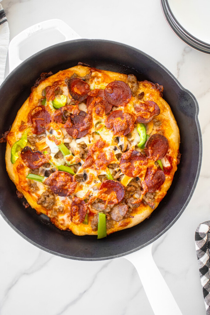 crispy crust pan pizza in a cast iron skillet on a white marble counter.