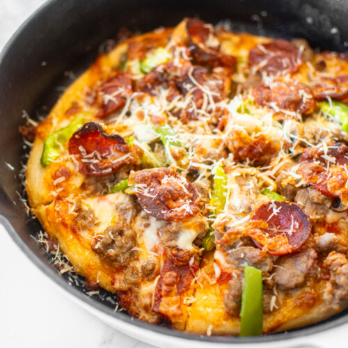 crispy crust pan pizza in a cast iron skillet on a white marble counter.