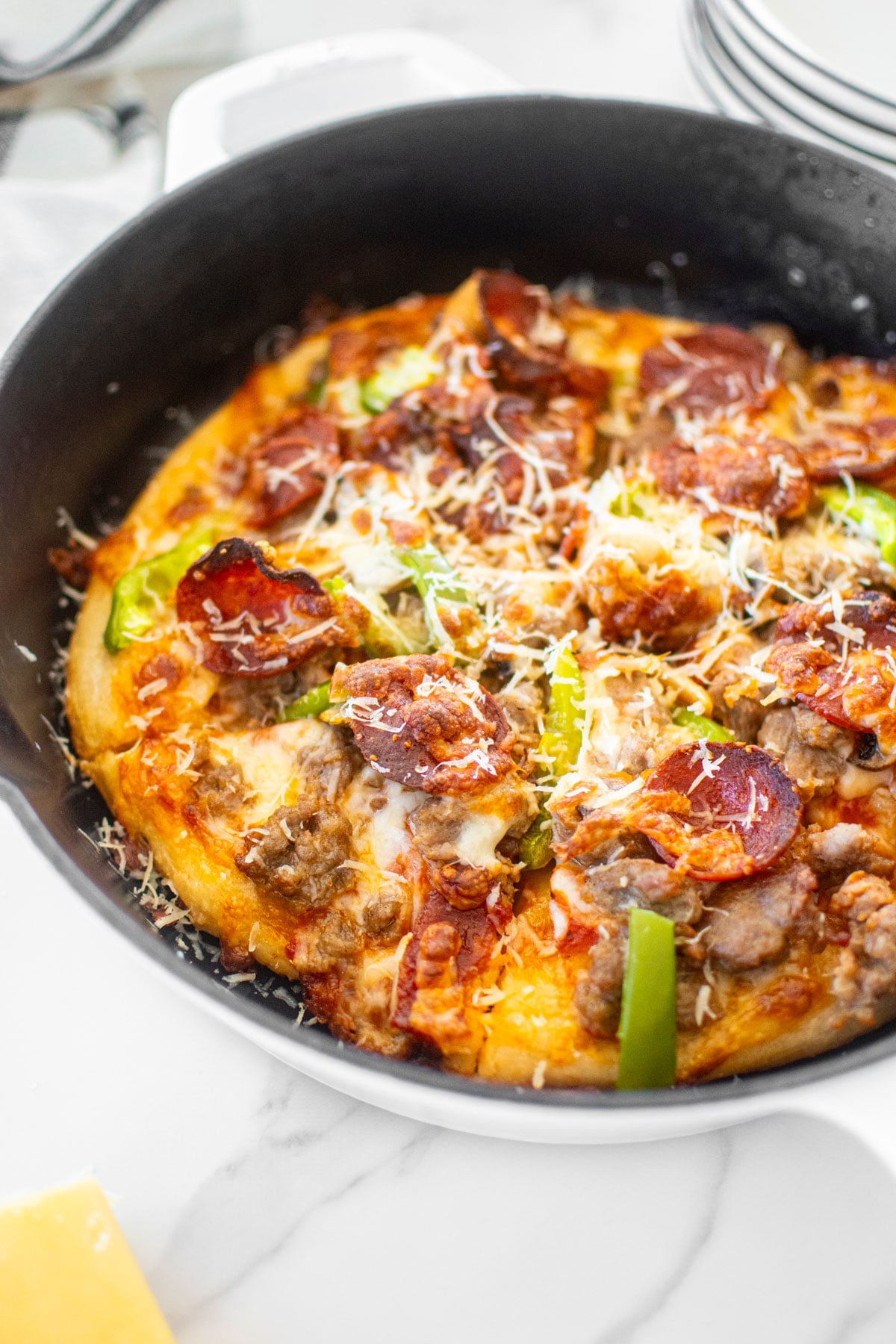 crispy crust pan pizza in a cast iron skillet on a white marble counter.