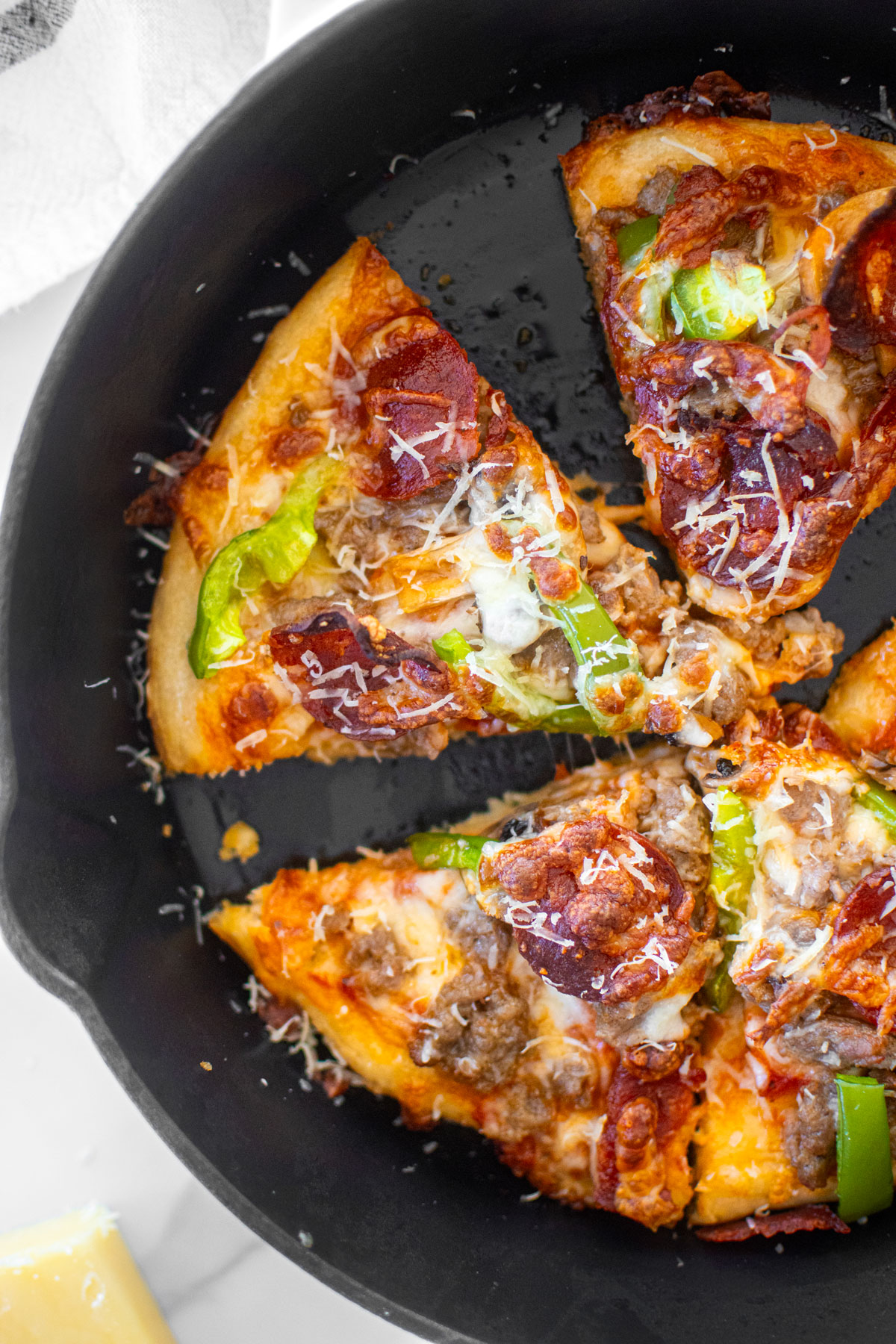 crispy crust pan pizza in a cast iron skillet cut into slices on a white marble counter.