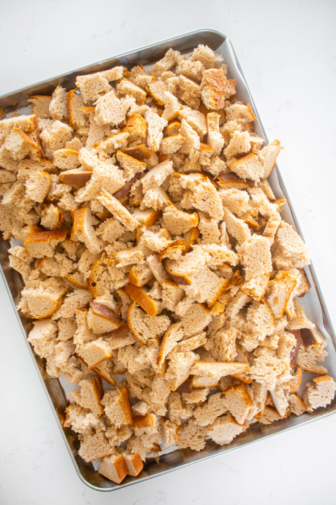 baking sheet of broken whole wheat bread pieces on a white marble counter.
