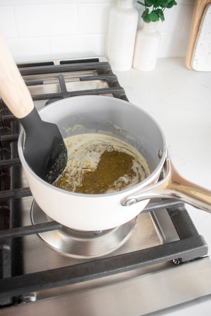 butter and herbs melting in a small pot on a stovetop.