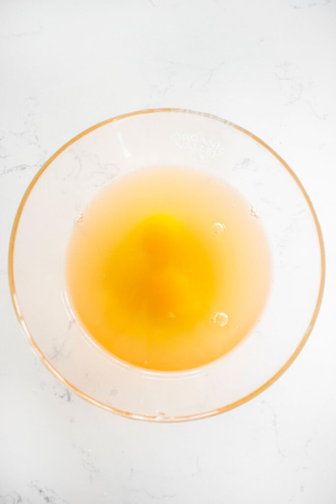 eggs and chicken broth in a glass mixing bowl on a white marble counter.