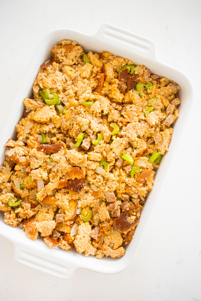 stuffing being added to a white ceramic dish on a white marble counter.