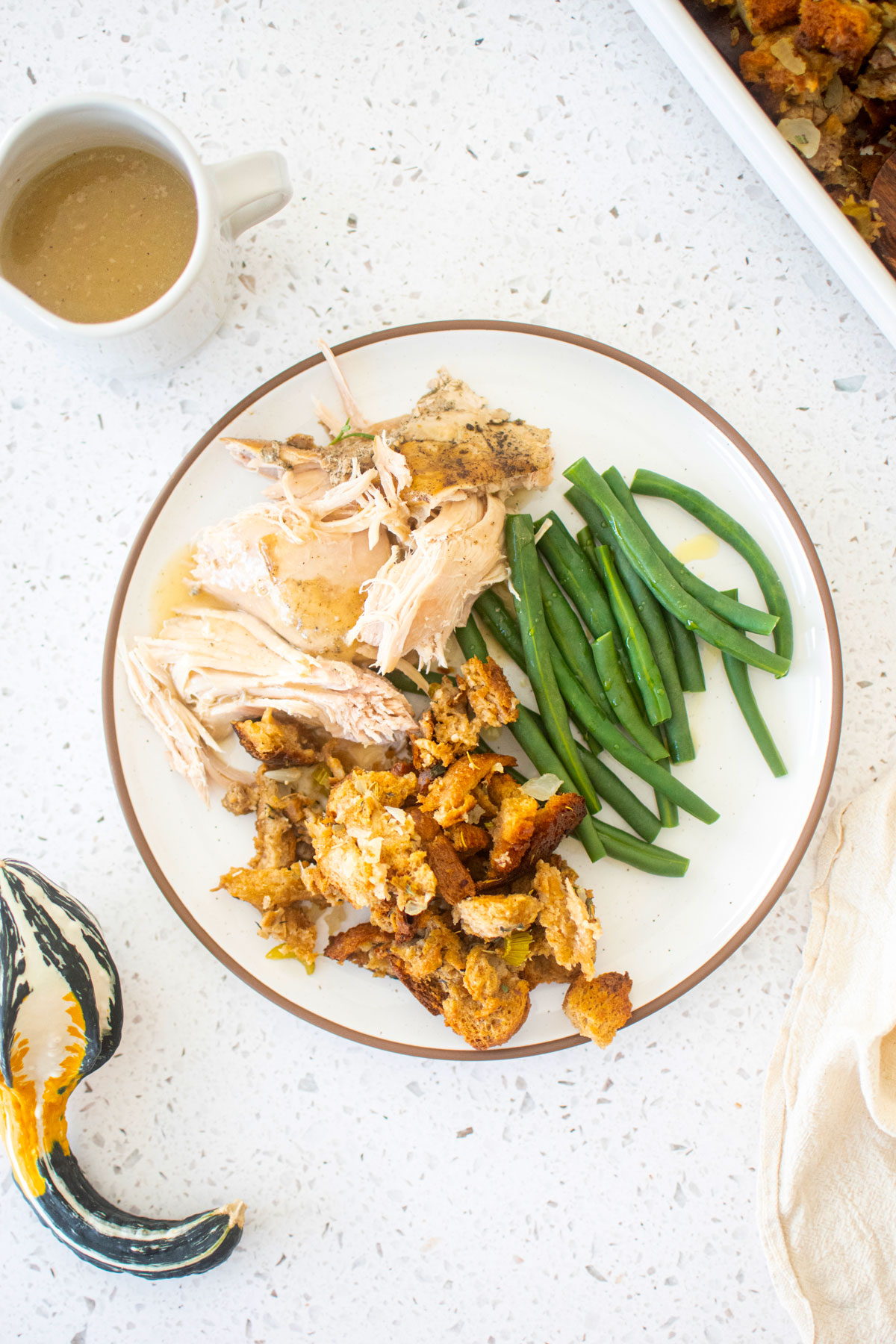 plate of turkey, stuffing and green beans on a white marble table.