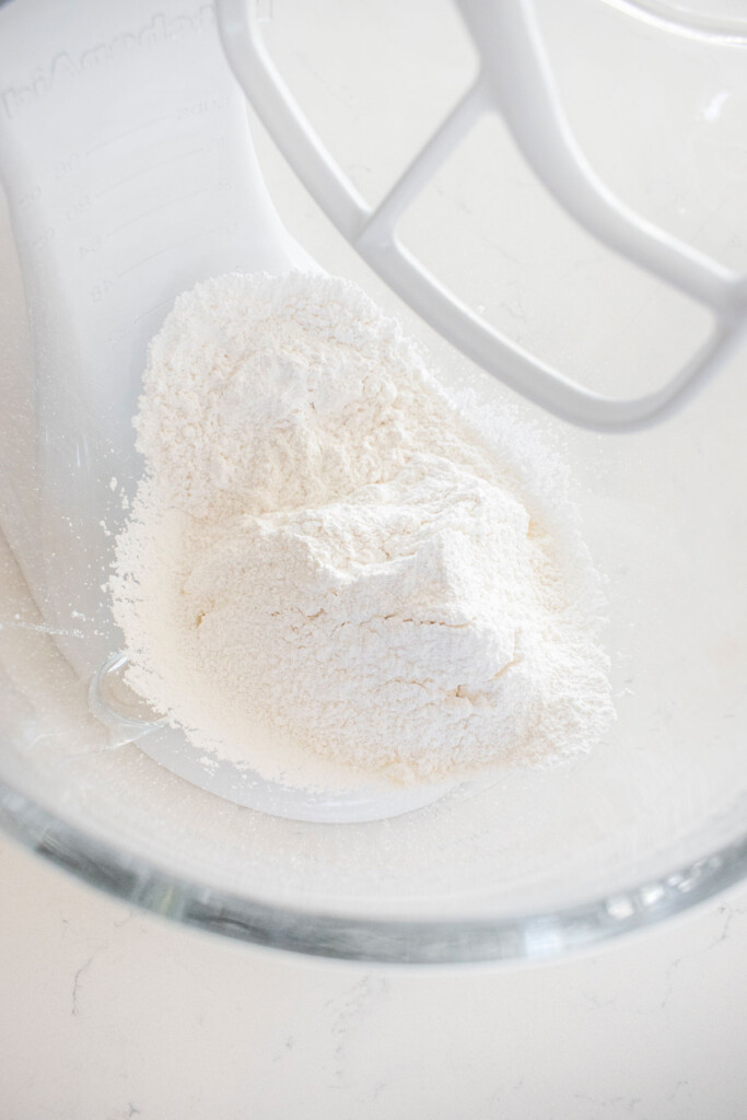 ingredients for vanilla frosting in a glass mixing bowl on a white marble counter.