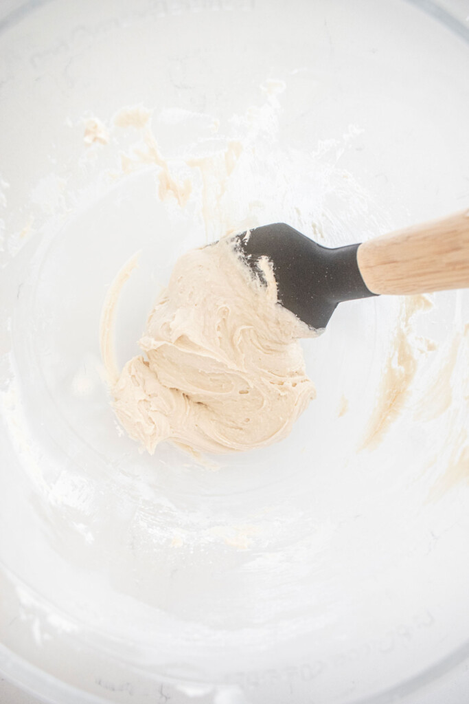vanilla frosting in a glass mixing bowl on a white marble counter.