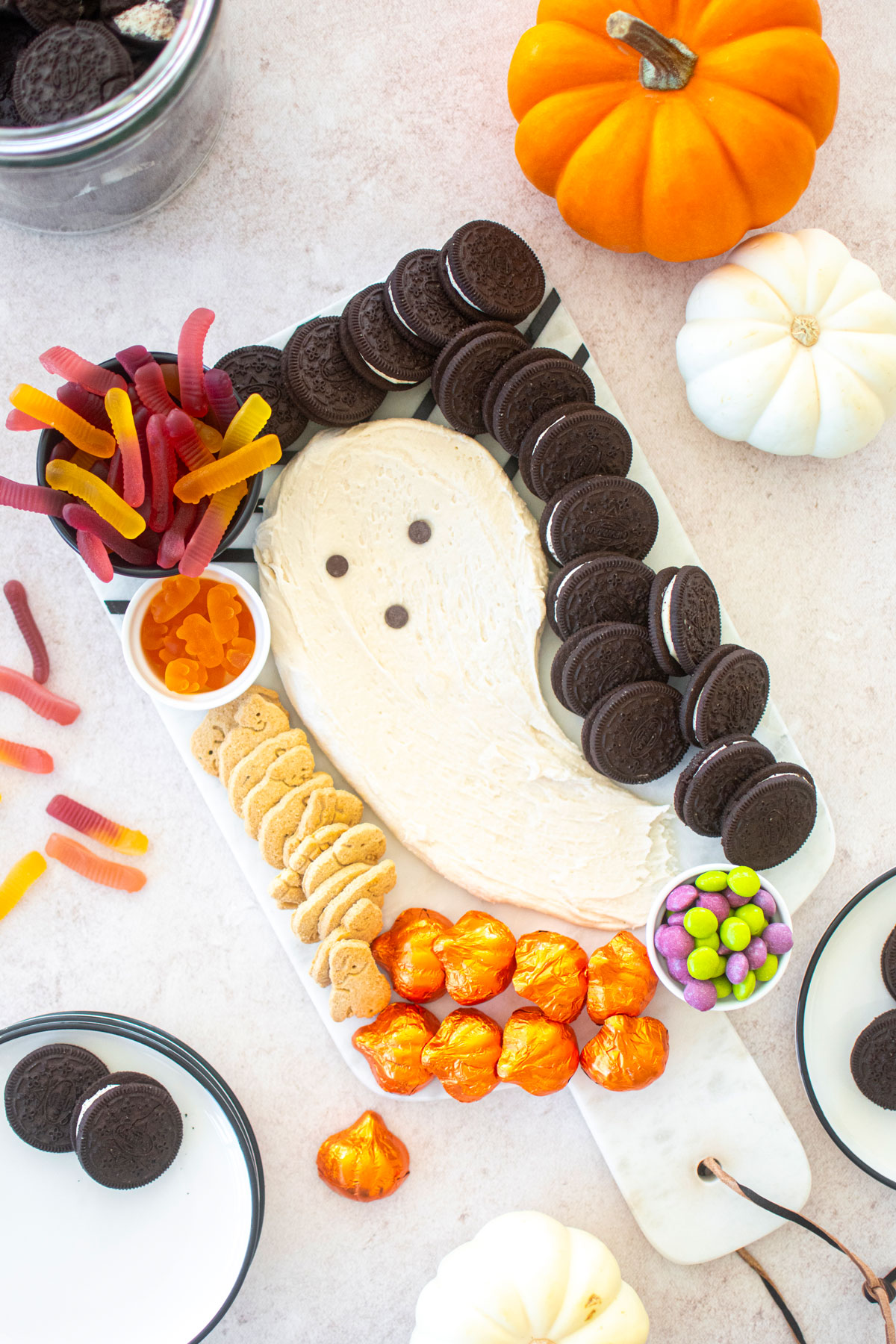 halloween dessert board with candy, a ghost frosting centerpiece and cookies on a table with pumpkins.