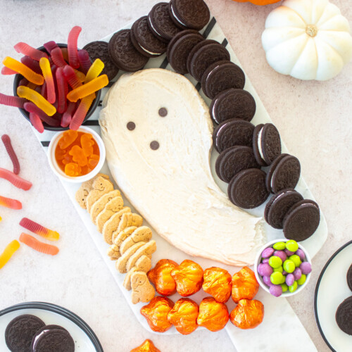 halloween dessert board with candy, a ghost frosting centerpiece and cookies on a table with pumpkins.