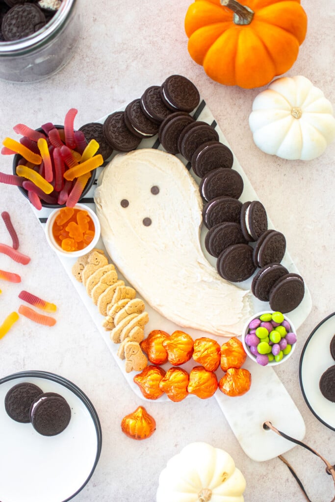 halloween dessert board with candy, a ghost frosting centerpiece and cookies on a table with pumpkins.