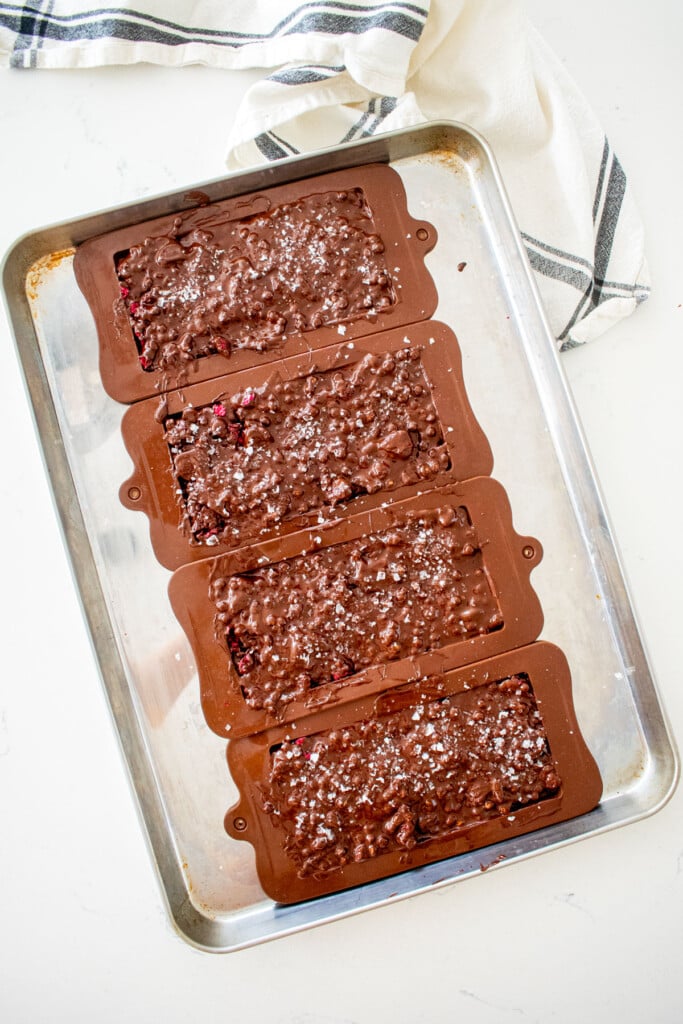baking sheet on a marble counter with chocolate bar molds filled with melted chocolate mixture.