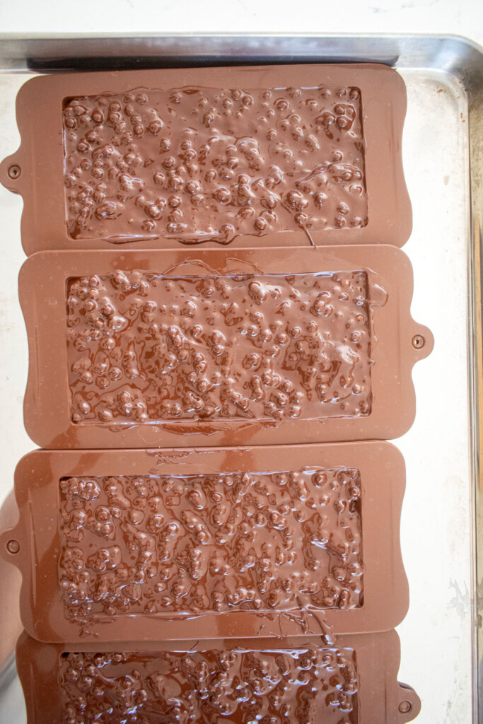 homemade crunch bars in chocolate bar molds on a baking sheet.