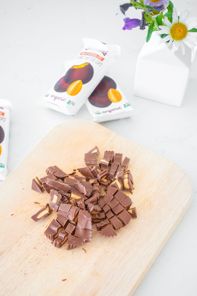 wood cutting board with chopped milk chocolate peanut butter cups on a marble counter.