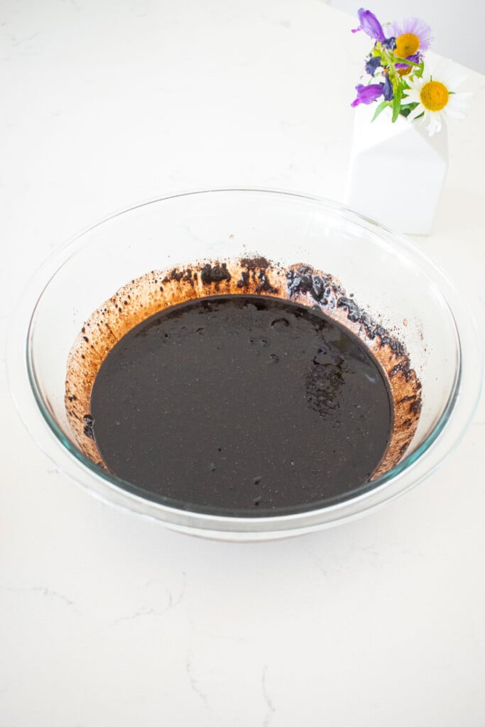 wet ingredients mixed together in a glass mixing bowl on a marble counter.