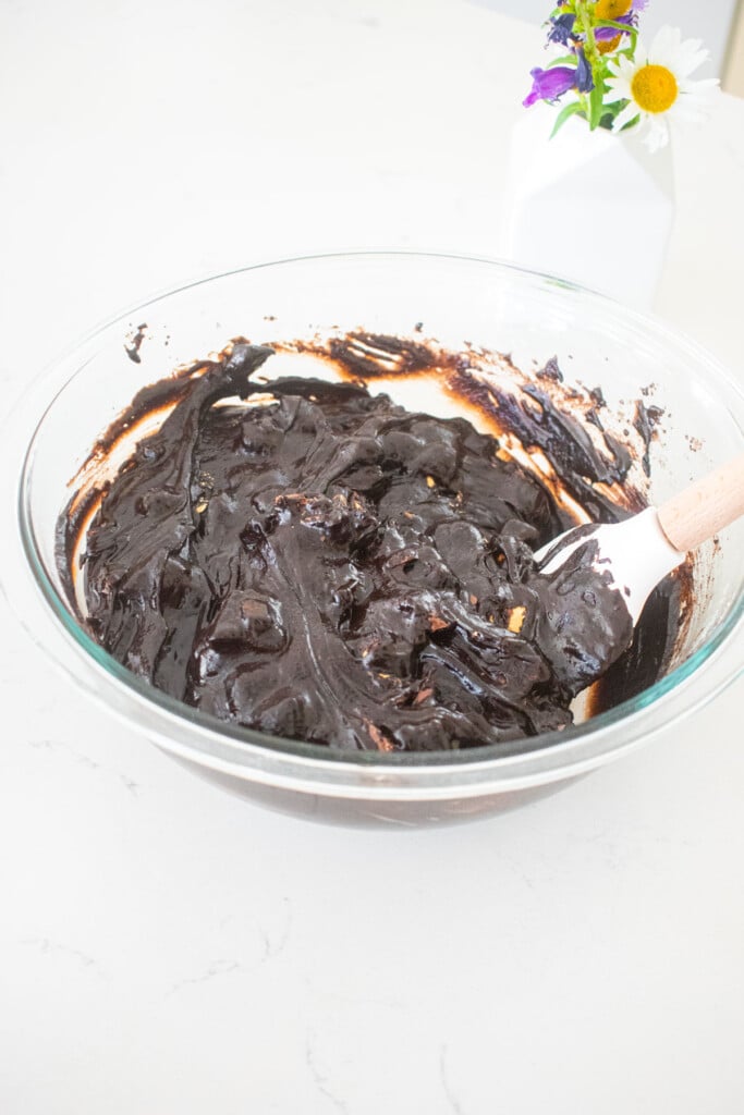 peanut butter cup brownie batter in a glass mixing bowl with a spatula on a marble counter.