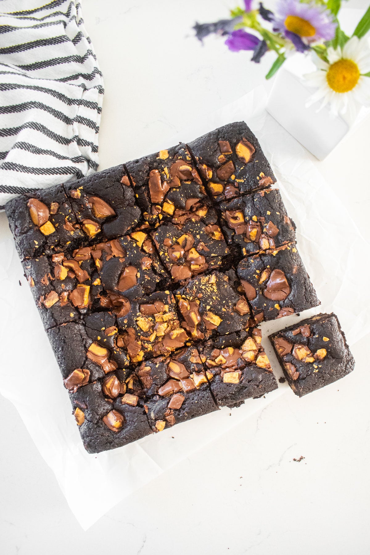 peanut butter cup brownies cut into small squares on a marble counter with fresh flowers.