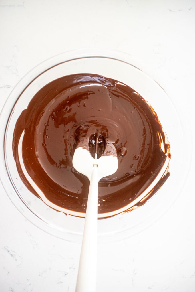 melted chocolate in a glass mixing bowl on a white marble counter.