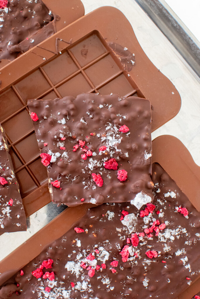 raspberry crunch bars on a baking sheet being pulled out of chocolate molds.