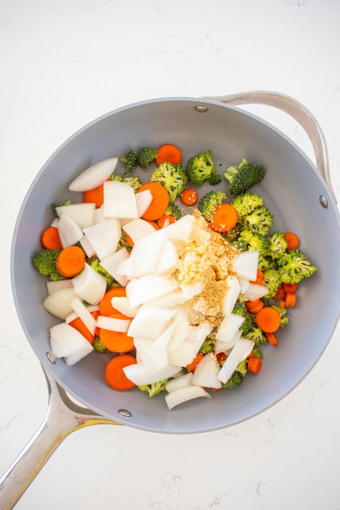 skillet with veggies, garlic, and ginger on a white marble countertop.