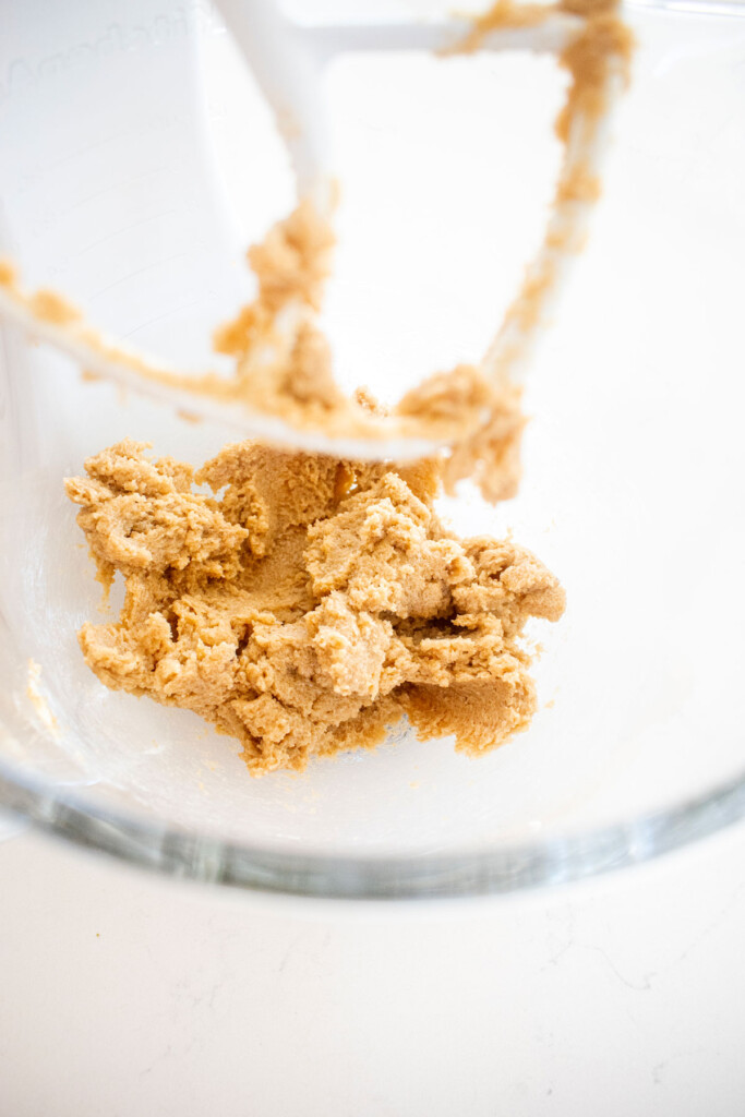 creamed vegan butter and sugar in a glass mixing bowl on a white marble counter.