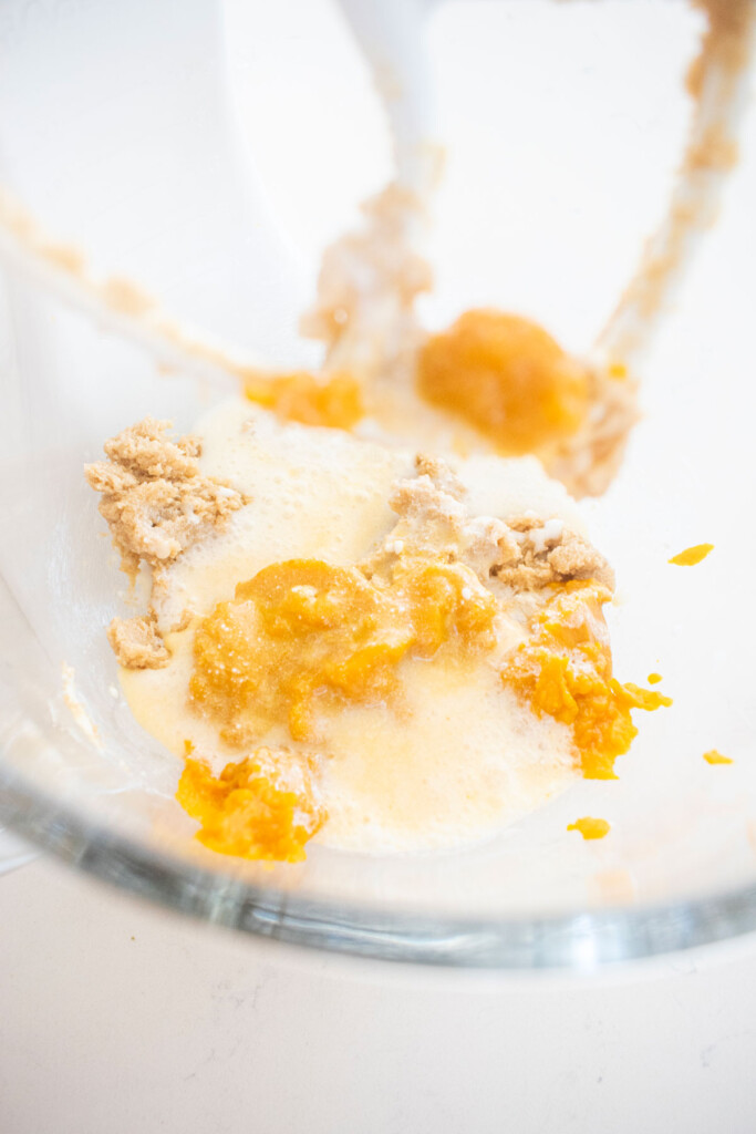 vegan pumpkin cupcakes being mixed together in a glass mixing bowl on a white marble counter.