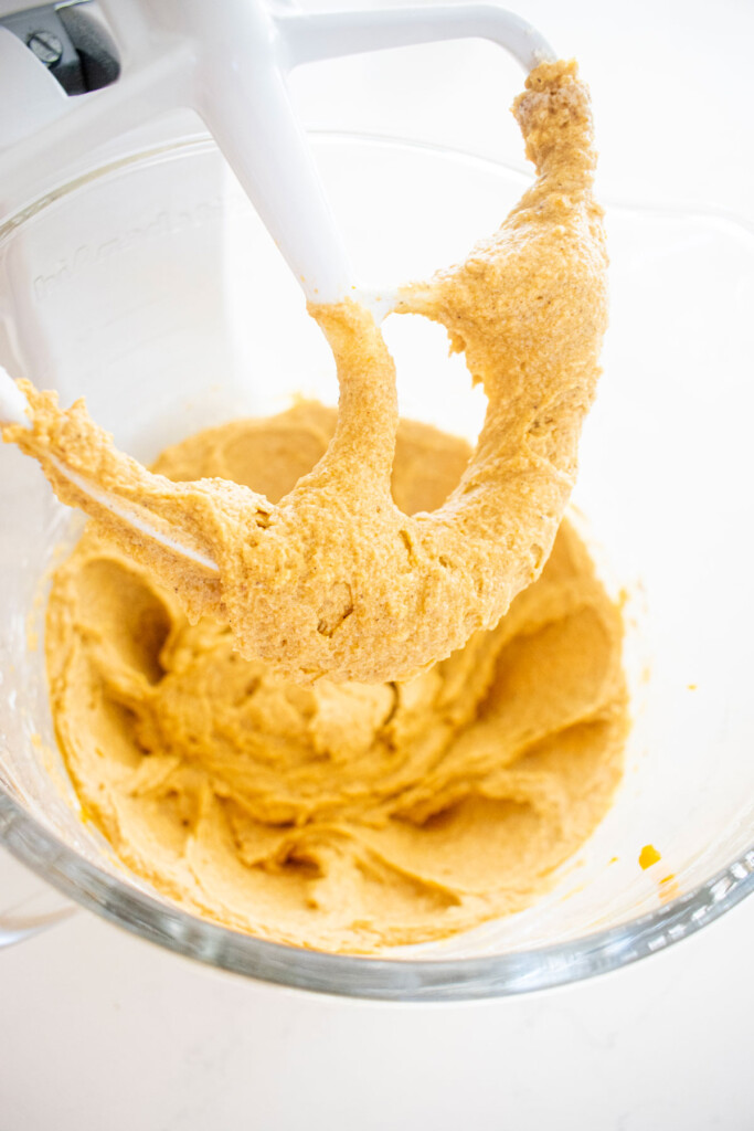 vegan pumpkin cupcake batter in a glass mixing bowl on a white marble counter.