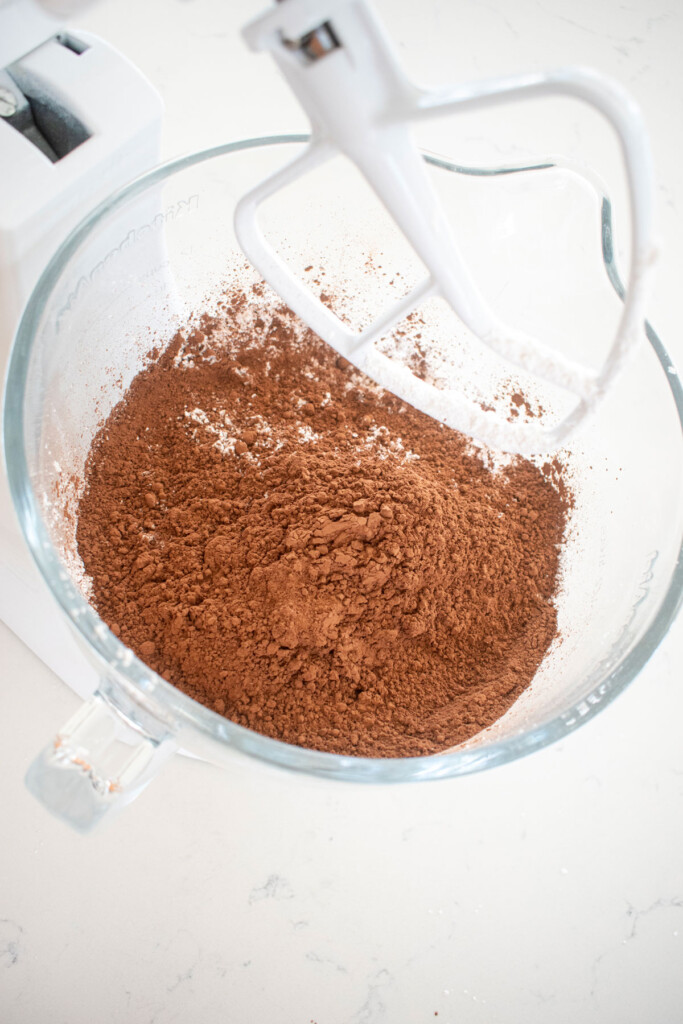 ingredients for vegan chocolate frosting in a glass mixing bowl on a white marble counter.