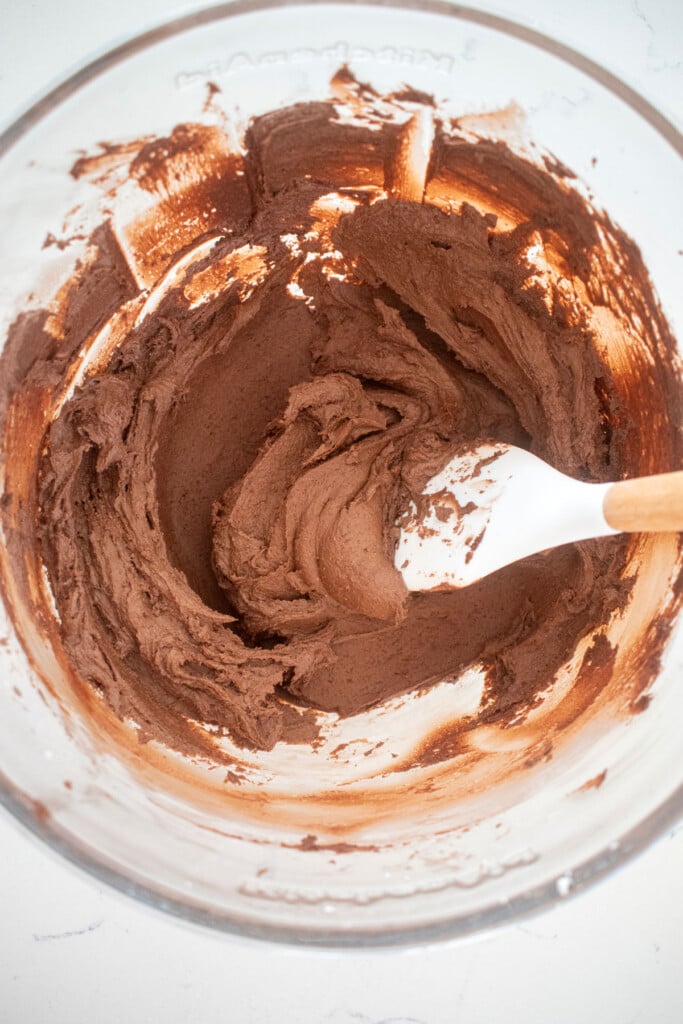 veagn chocolate frosting in a glass mixing bowl on a white marble counter.