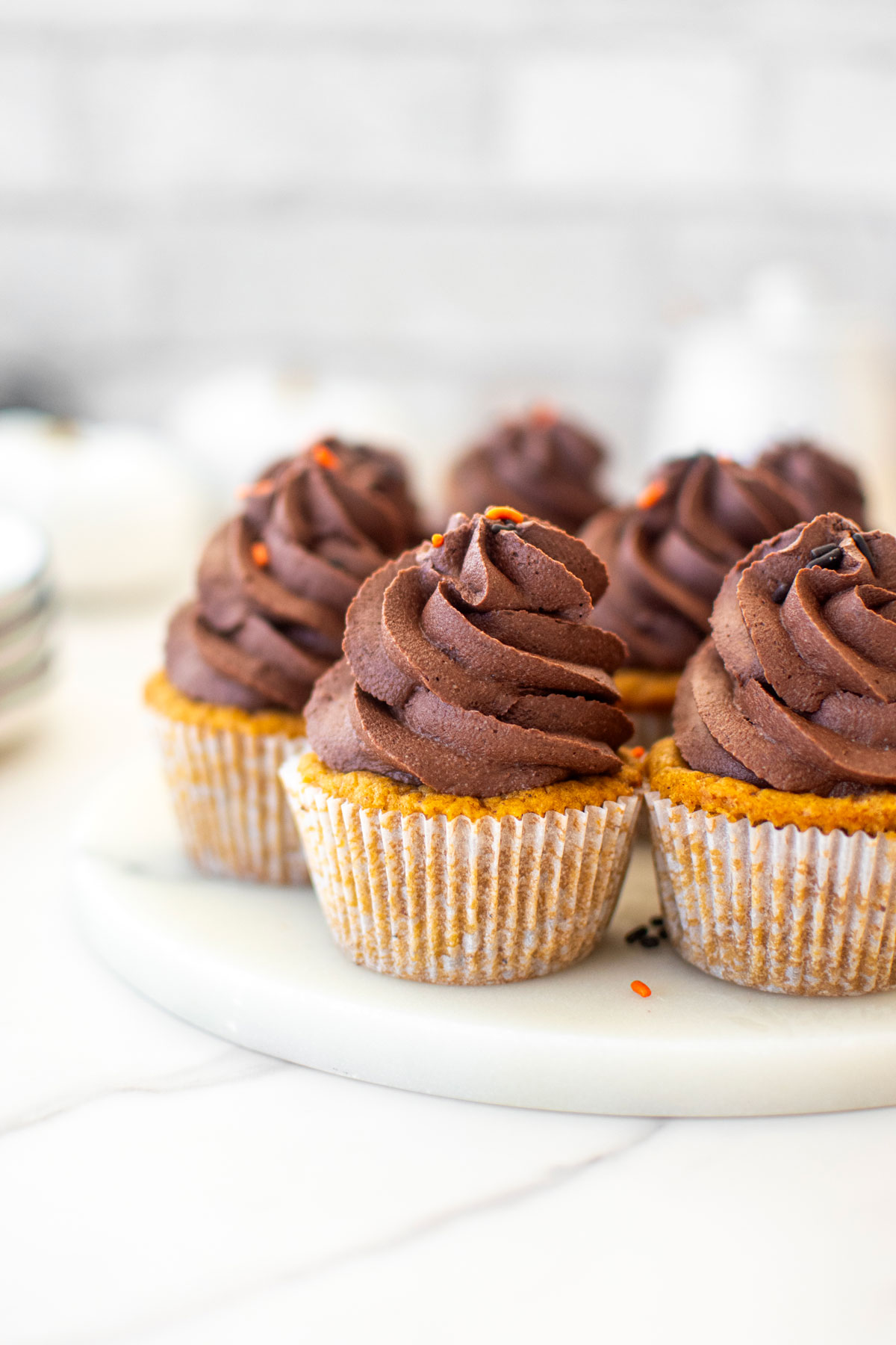 vegan pumpkin cupcakes with chocolate frosting on a marble serving board.