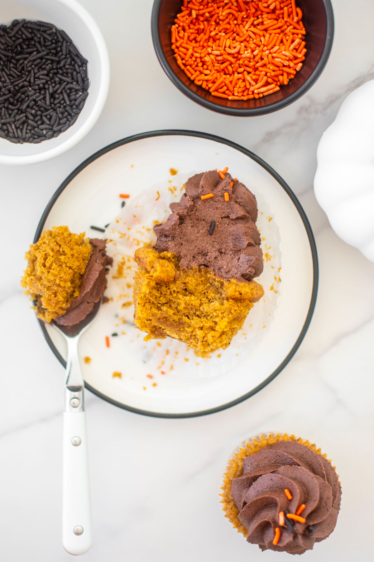 vegan pumpkin cupcake with chocolate frosting on a white plate with a bite taken out.