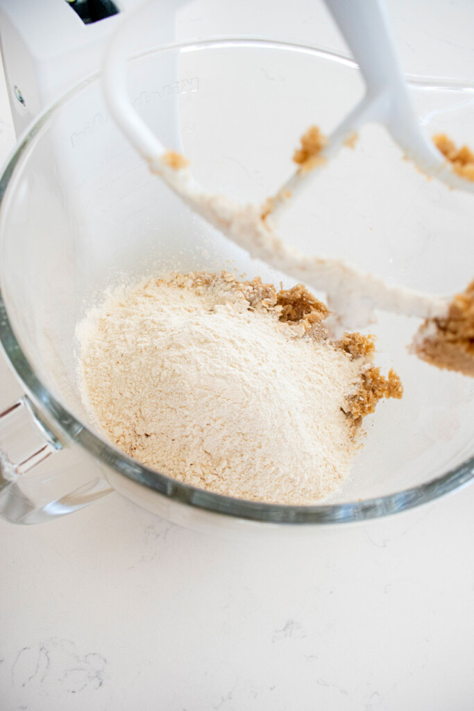ingredients for vegan spiced oatmeal raisin cookies in a glass mixing bowl on a white marble counter.
