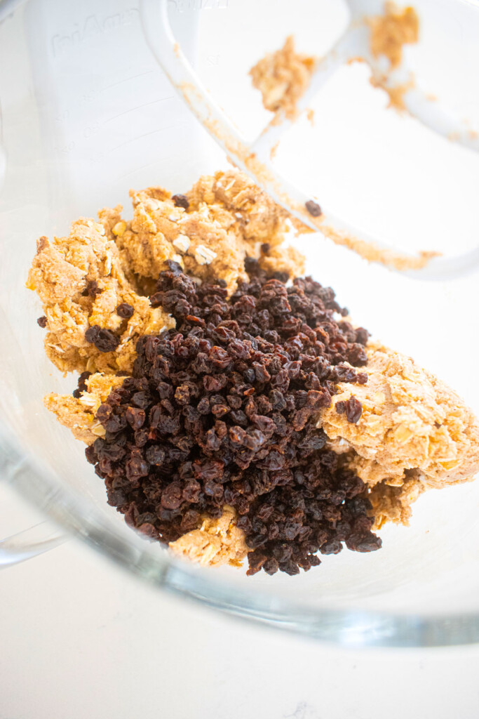 vegan spiced oatmeal cookie dough with raisins in a glass mixing bowl.
