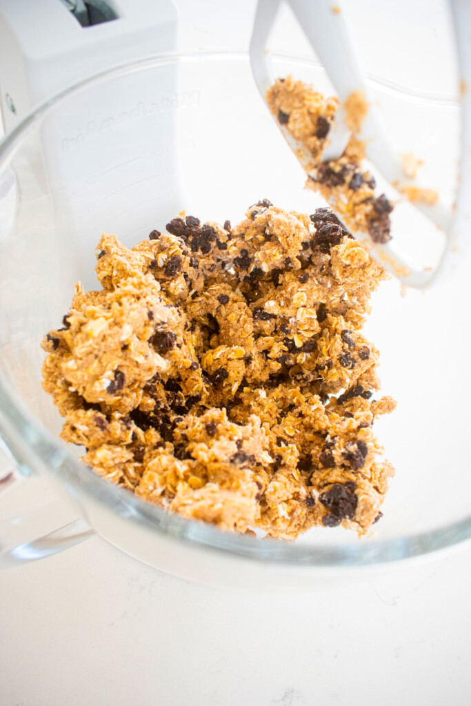 vegan spiced oatmeal raisin cookie dough in a glass mixing bowl on a white marble counter.