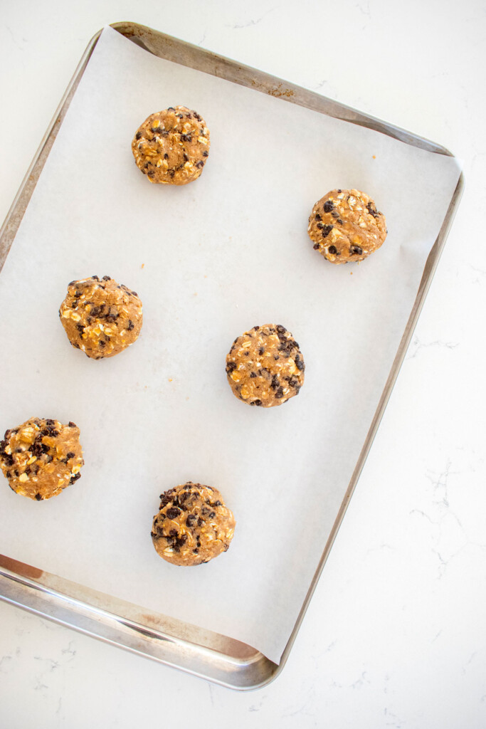 vegan spiced oatmeal raisin cookie dough balls on a baking sheet on a white marble counter.