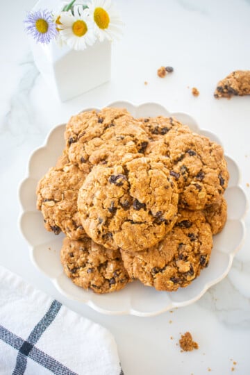 veagn spiced oatmeal raisin cookies on a plate on a marble counter with fresh flowers.