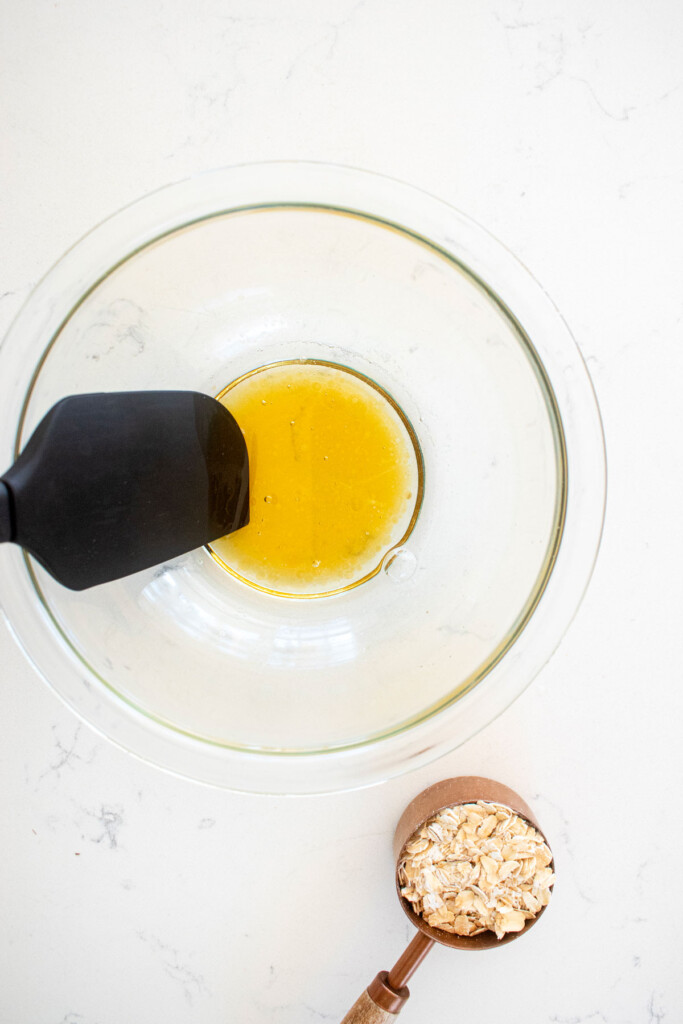 melted coconut oil and honey in a glass mixing bowl on a white marble countertop.