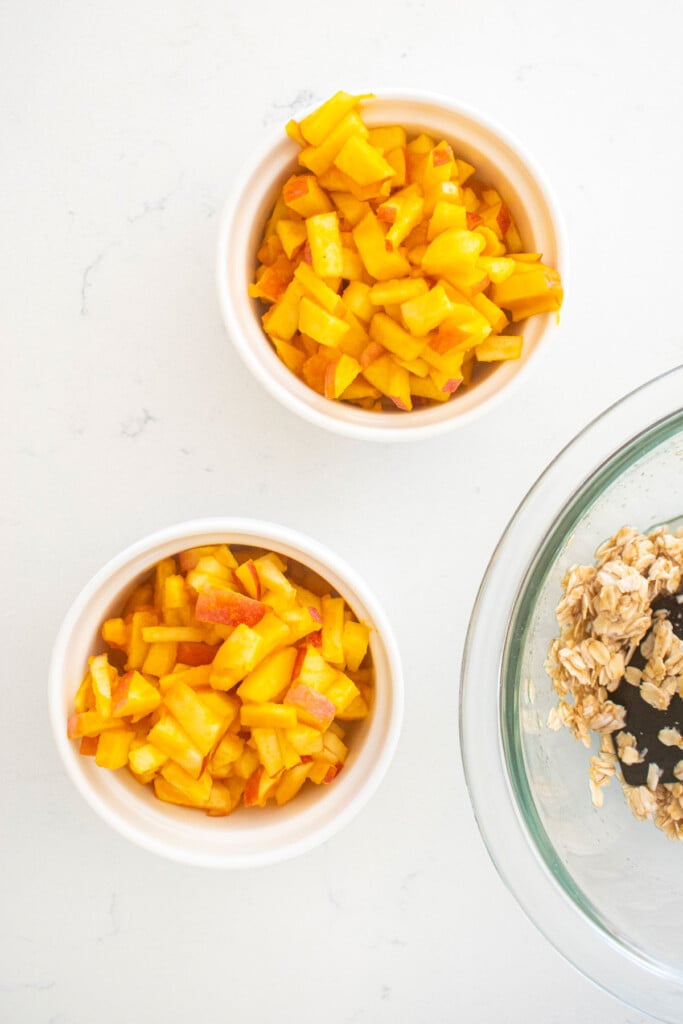 two white ramekins with apple and pumpkin mixture sitting on a white marble countertop.