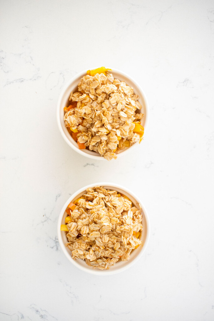two ramekins of apple crisp for dogs sitting on a white marble countertop.