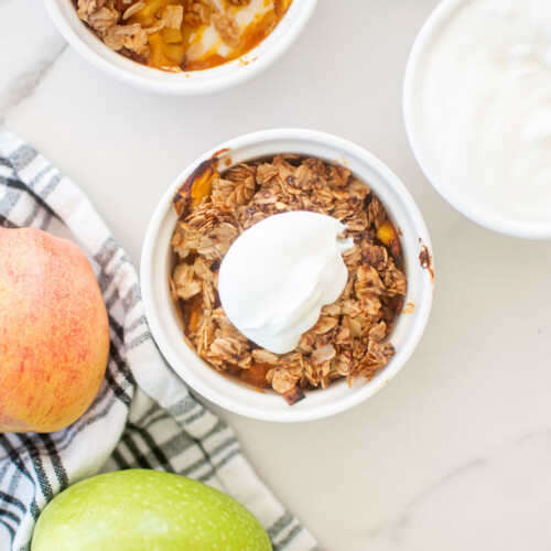 apple crisp for dogs in a white ramekin with a dollop of greek yogurt on top sitting on a white marble countertop.