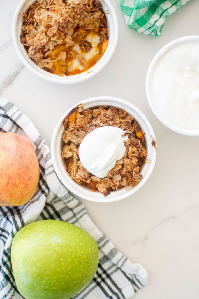 apple crisp for dogs in a white ramekin with a dollop of greek yogurt on top sitting on a white marble countertop.