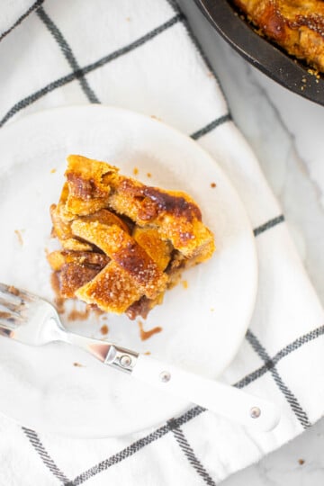 brown butter apple pie slice on a white plate on a white and black check kitchen towel.